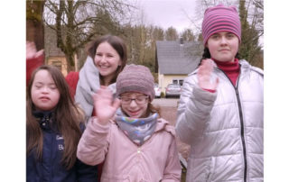 Eine Freiwillige und drei Kinder winken lächelnd in die Kamera