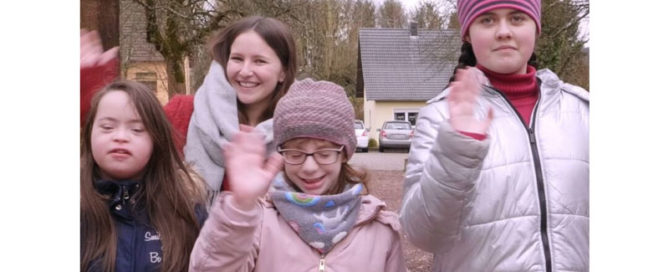 Eine Freiwillige und drei Kinder winken lächelnd in die Kamera