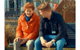 Ein Freiwilliger und eine late Dame sitzen auf einer Parkbank und unterhalten sich