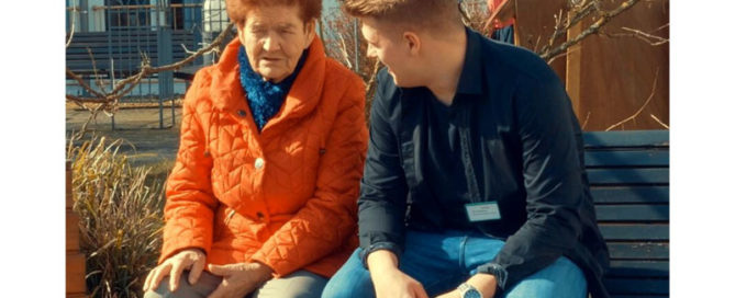 Ein Freiwilliger und eine late Dame sitzen auf einer Parkbank und unterhalten sich