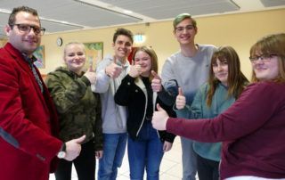 Sieben Freiwilligen lächeln in die Kamera und zeigen den erhobenen Daumen