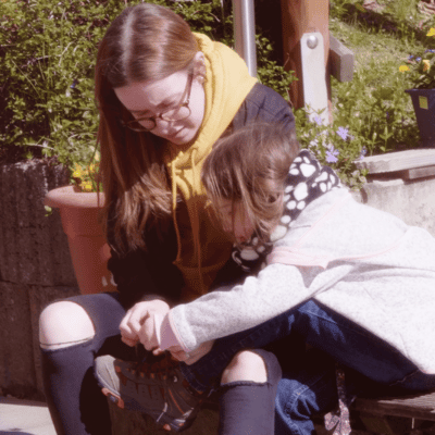 Eine junge Freiwillige hilft einem Mädchen beim Schuhe binden