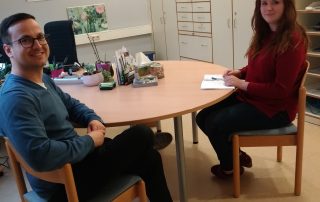 Dominik Steinmann sitzt mit einer FSJlerin am Tisch und beide lächeln in die Kamera