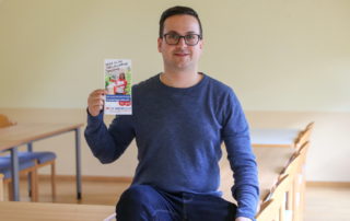 Dominik Steinmann hält einen Flyer der paritätischen Freiwilligendienste in die Kamera