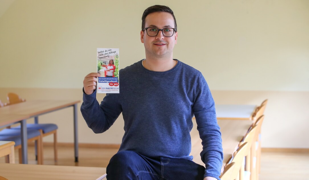 Dominik Steinmann hält einen Flyer der paritätischen Freiwilligendienste in die Kamera