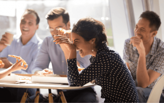 vier Personen sitzen an einem Tisch, essen gemeinsam Pizza und lachen
