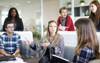 sechs Personen im Arbeitskontext diskutieren miteinander