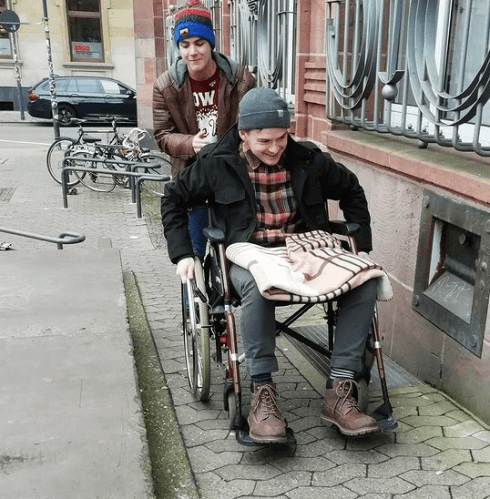 Ein Freiwilliger schiebt einen anderen Freiwilligen im Rollstuhl eine Rampe hoch
