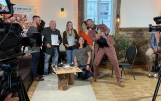 Mehrere Freiwillige, die Leitungungen des Kompetenzzentrums Freiwilligendienste und der Moderator Kalibo machen zusammen ein Selfie. Die Freiwilligen halten dabei ihre Urkunden in die Hand.