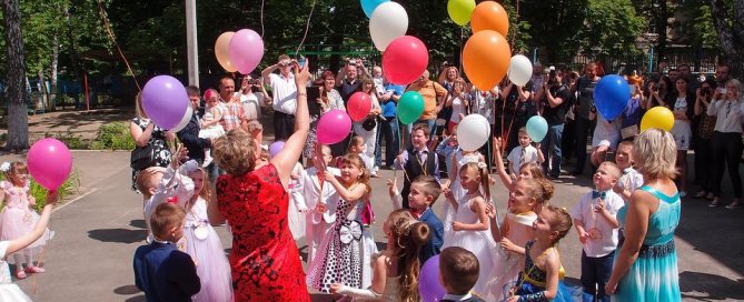 Viele Kinder, die zusammen stehen und bunte Luftballons in die Luft steigen lassen.